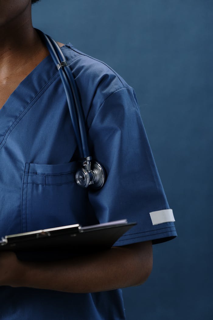 Services-03 Close-up of a healthcare professional in blue scrubs with a stethoscope and clipboard.